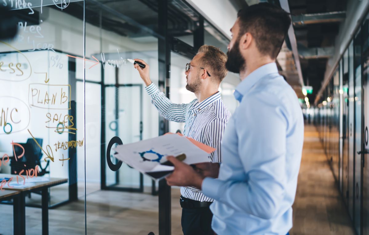 Two man brainstorming ideas on a glass board